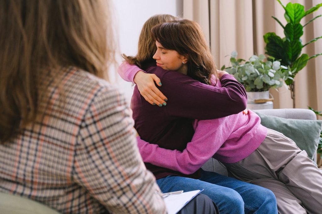 couple-hugging-during-session-with-psychologist-7176224 Side view of couple sitting on sofa and embracing during session with psychologist in light room in daytime